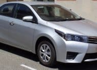Front three-quarter view of a silver Toyota sedan parked on a street, with the license plate visible in the front bumper.