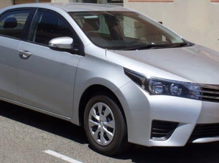 Front three-quarter view of a silver Toyota sedan parked on a street, with the license plate visible in the front bumper.