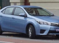 Blue Toyota sedan parked on the street, front-right view, license plate visible (1GCM-030).