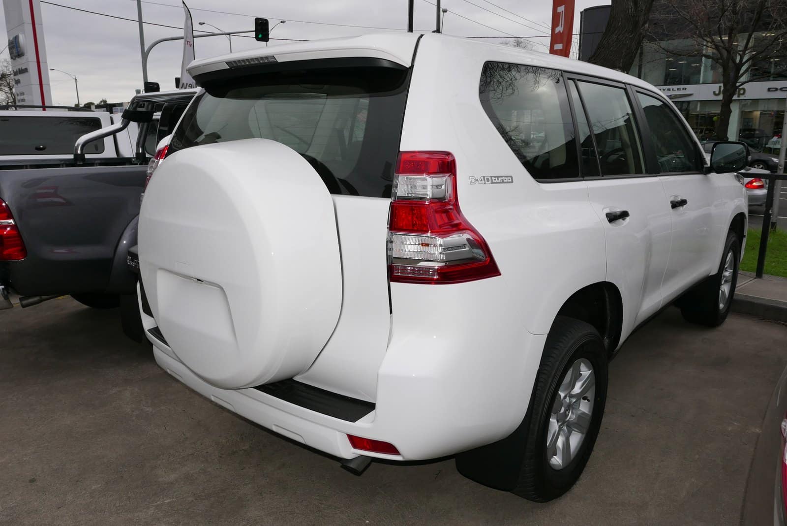 White SUV with a rear-mounted spare tire cover on a dealership lot, showing a D-4D turbo badge on the tailgate.