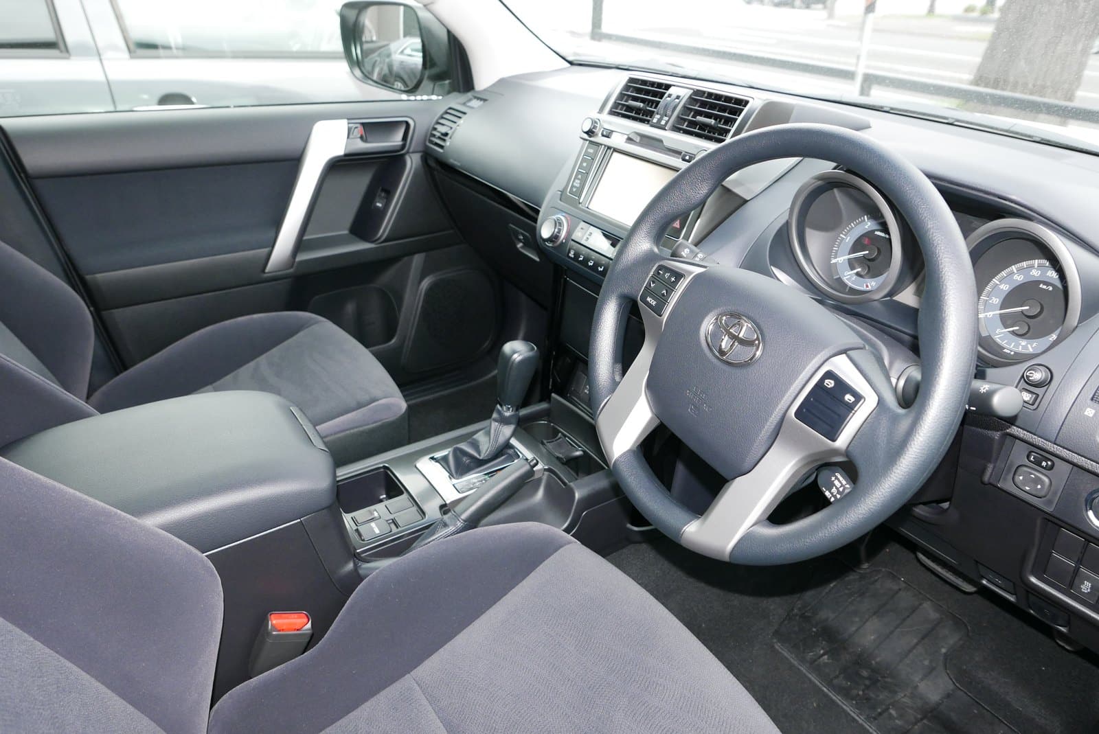Interior of a car showing the driver's seat, steering wheel, center console, and dashboard controls as seen from the passenger side perspective.