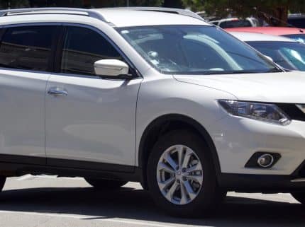 White Nissan SUV parked in a parking lot, front and side view showing the vehicle's grille and headlights.