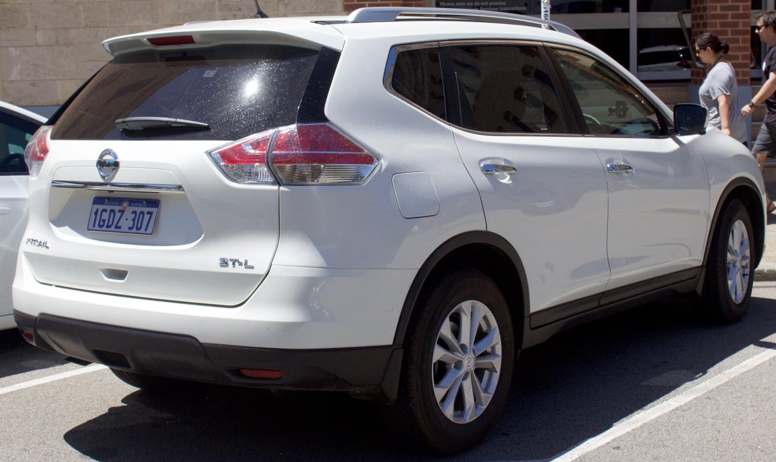White Nissan Murano SUV shown from the rear-three-quarters, parked in a parking lot with a storefront and pedestrians in the background.
