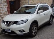 Front three-quarter view of a white Nissan SUV parked along a stone building wall, with roof rails visible.