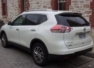 White Nissan X-Trail SUV parked, rear three-quarter view with tinted windows and roof rails.