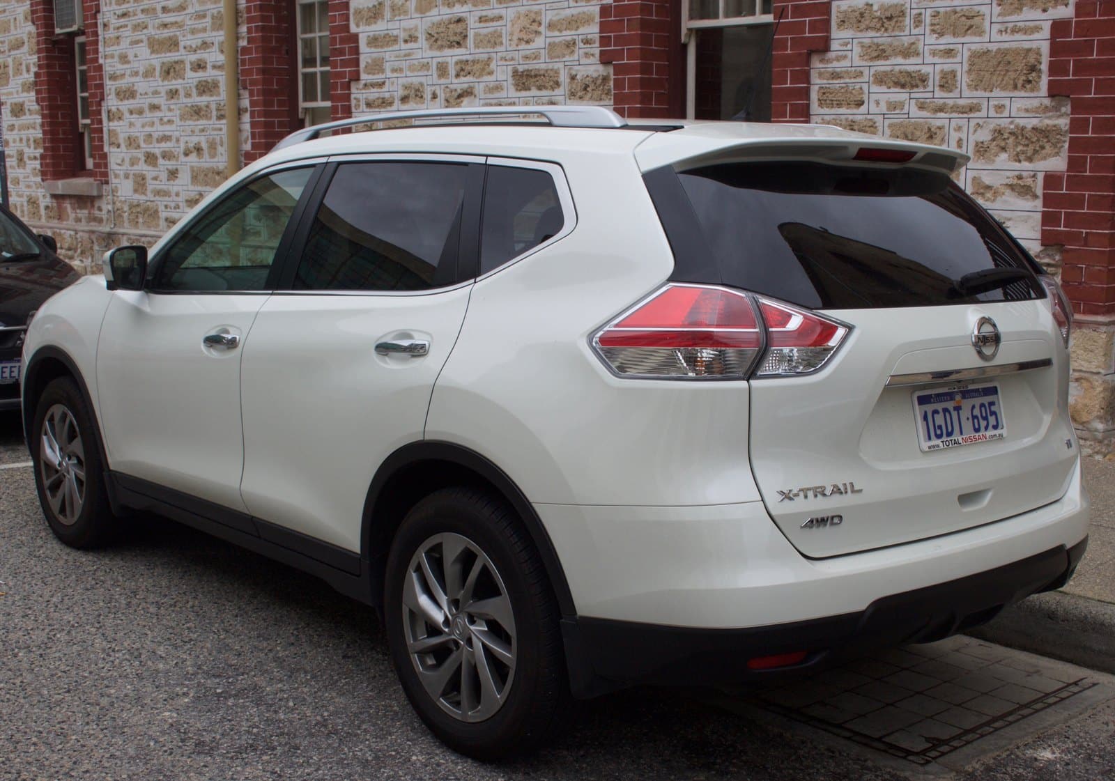 White Nissan X-Trail SUV parked, rear three-quarter view with tinted windows and roof rails.