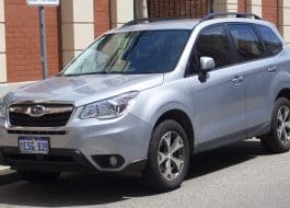 Front-right view of a silver Subaru SUV parked along a city street, brick building in background, license plate 1ESG-839 visible