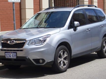 Front-right view of a silver Subaru SUV parked along a city street, brick building in background, license plate 1ESG-839 visible