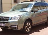 Light green Subaru SUV parked on a sunny street, front three-quarter view showing grille, headlights, and roof rails.