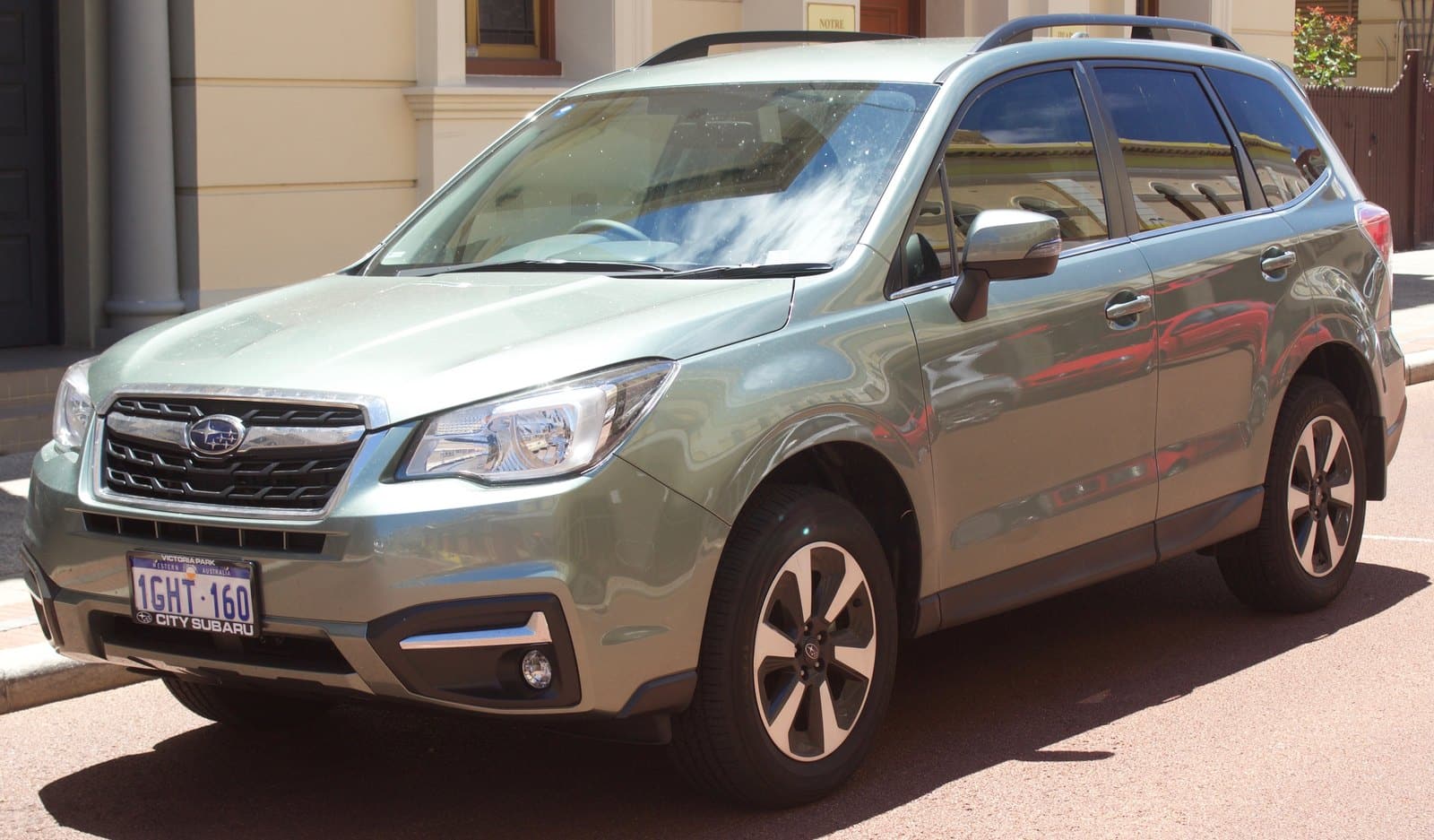 Light green Subaru SUV parked on a sunny street, front three-quarter view showing grille, headlights, and roof rails.