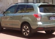 Rear three-quarter view of a light blue Subaru Forester SUV parked on a city street, with roof rails and visible license plate balance on the rear.