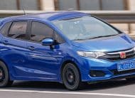Blue Honda compact car driving quickly on a highway, license plate L D7C65, with a blurred guardrail background.