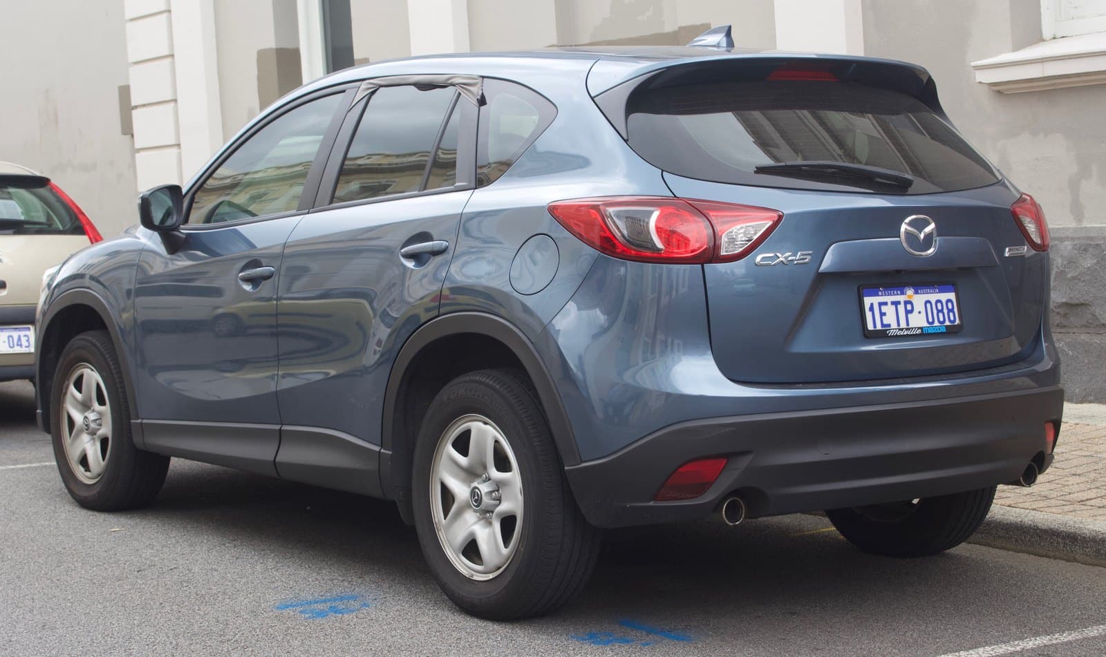 Blue Mazda CX-5 SUV parked on a city street, shown from the rear three-quarters with license plate visible.