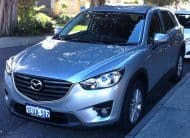 Silver Mazda SUV parked on a street, front-left angle, showing the grille and headlights.