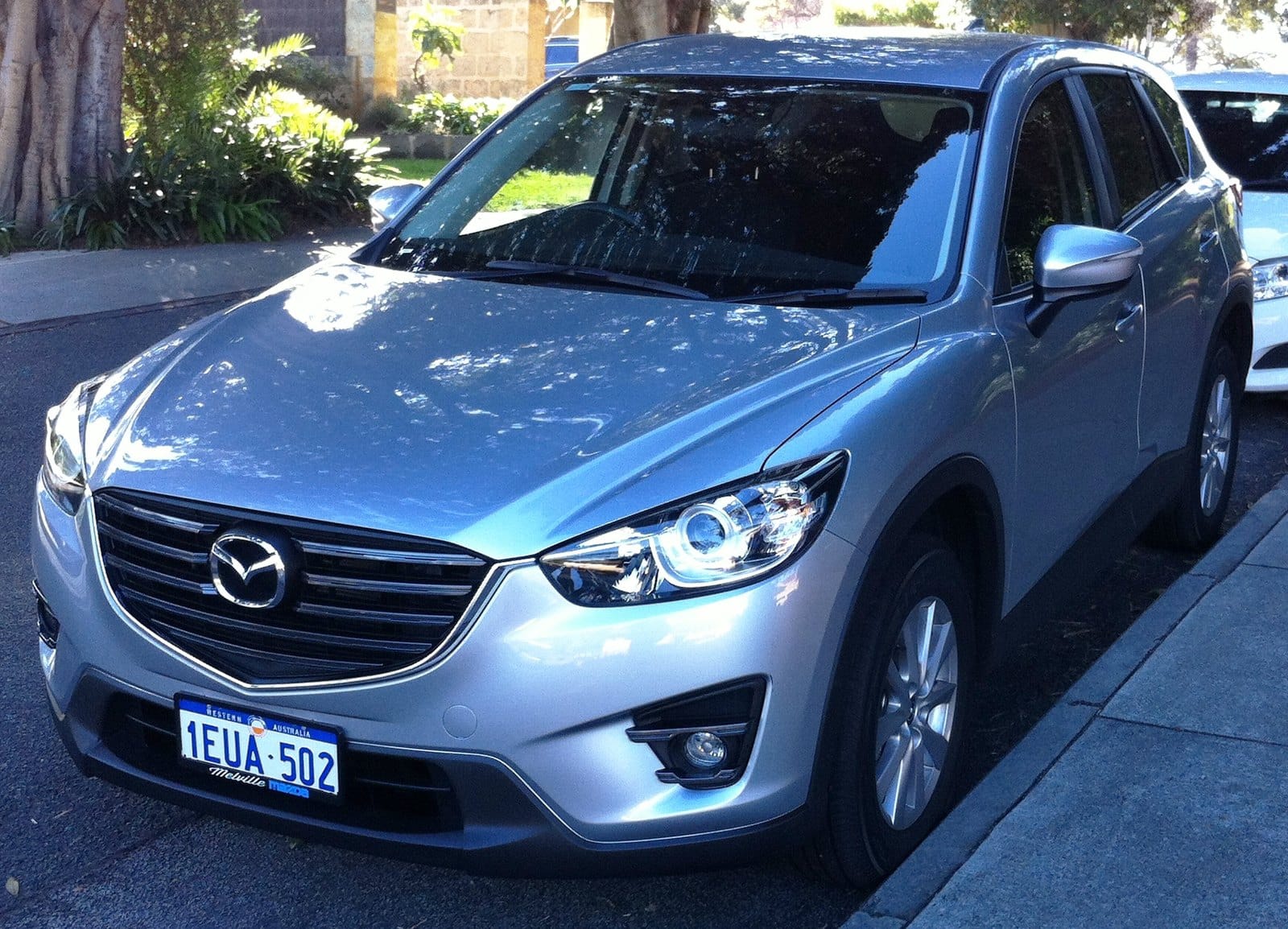 Silver Mazda SUV parked on a street, front-left angle, showing the grille and headlights.